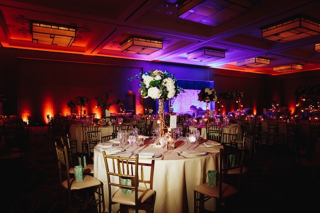 Salão de banquetes decorado com mesa redonda servida com peça central de hortênsia e cadeiras chiavari