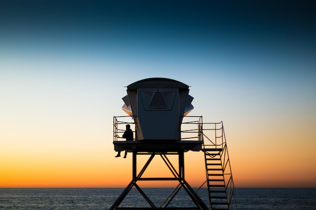 Foto grátis salva-vidas na praia na torre de vigia ao pôr do sol