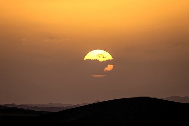 Foto grátis silhueta de dunas de areia com o sol atrás de uma nuvem