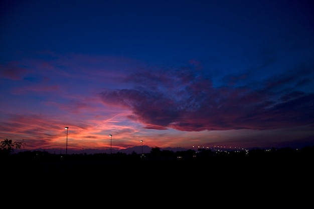 Silhuetas de colinas e postes de luz sob um céu nublado durante um lindo pôr do sol