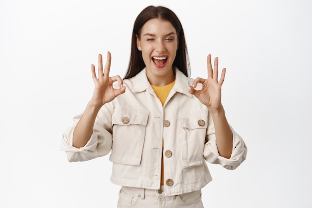 Foto grátis sim está bem. mulher sorridente feliz rindo e sorrindo, piscar enquanto mostra gesto de ok zero, garanta tudo sob controle, tudo bem, elogio, resultado garantido no branco