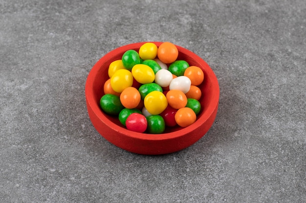 Foto grátis tigela vermelha de doces redondos coloridos na mesa de pedra.