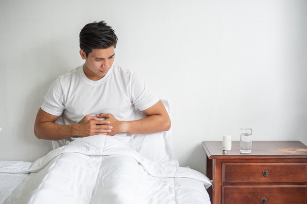 Foto grátis um homem está sentado na cama com dor de estômago e pressiona o estômago com as mãos.