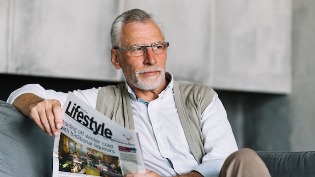 Um, homem idoso, sentar sofá, segurando jornal, em, seu, mão, olhando