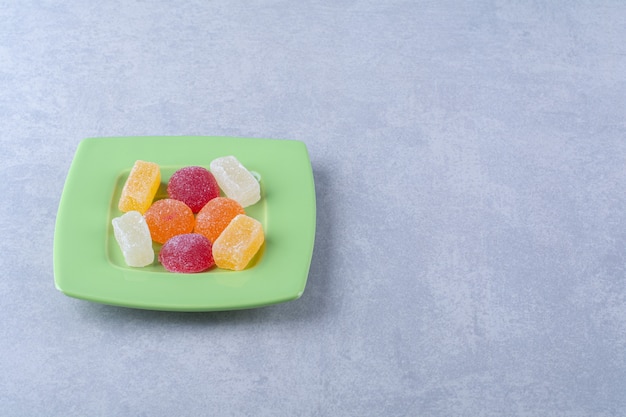 Foto grátis um prato verde cheio de balas de gelatina açucaradas na superfície cinza