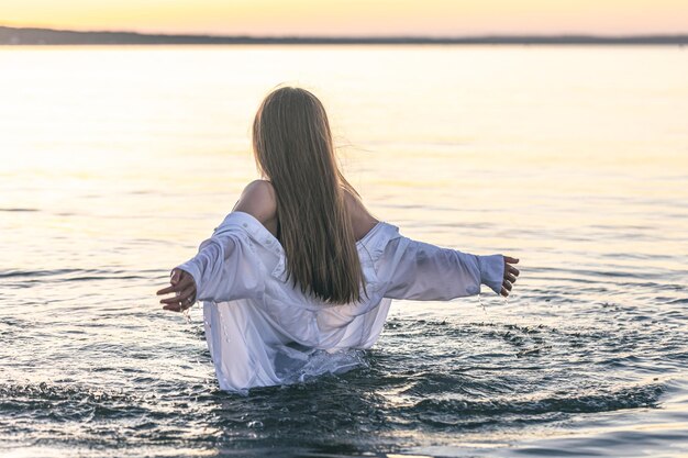 Uma mulher de maiô e camisa branca no mar ao pôr do sol