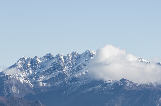 Vista de uma montanha rochosa coberta de neve parcialmente coberta por nuvens