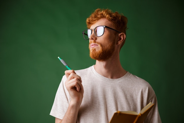 Foto grátis vista do close-up de pensar jovem barbudo em camiseta branca, segurando um caderno e uma caneta