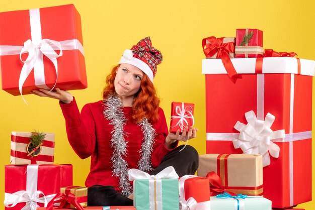 Vista frontal de uma jovem sentada ao redor do Natal apresenta-se na parede amarela