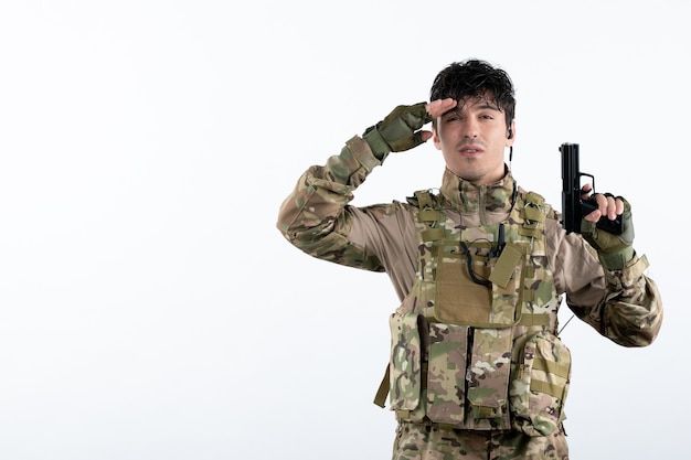 Foto grátis vista frontal do jovem soldado em uniforme militar com parede branca de arma de fogo