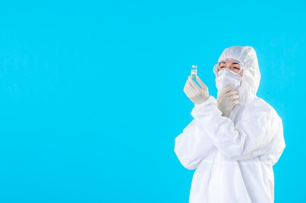 Foto grátis vista frontal do médico masculino em traje de proteção e máscara segurando um pequeno frasco em azul