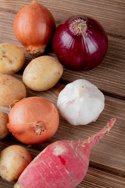 Foto grátis vista lateral de legumes como cebola batata alho e rabanete em fundo de madeira