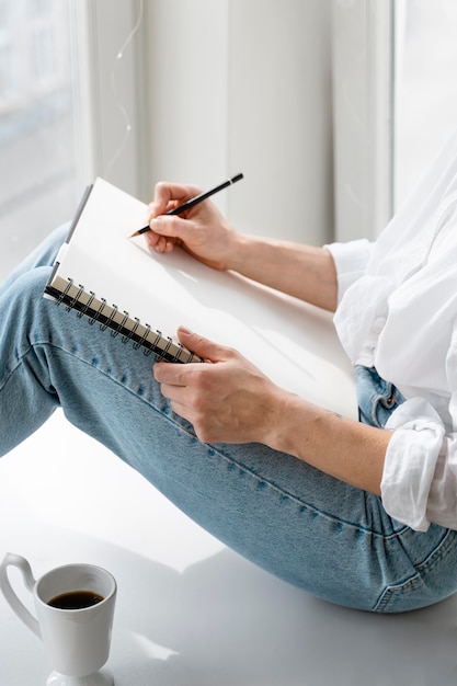 Foto grátis vista lateral de uma jovem mulher desenhando em casa perto da janela