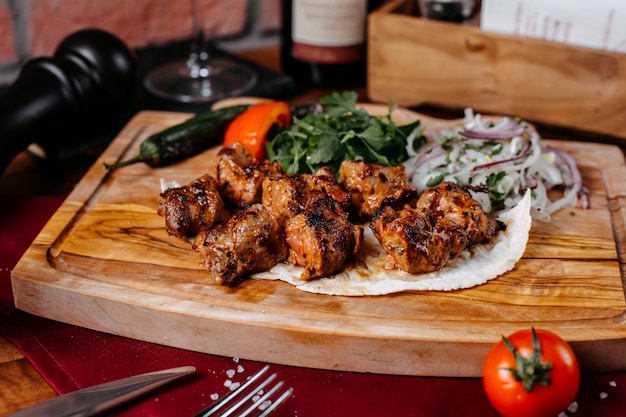 Foto grátis vista lateral do kebab de frango com cebola e ervas em uma placa de madeira