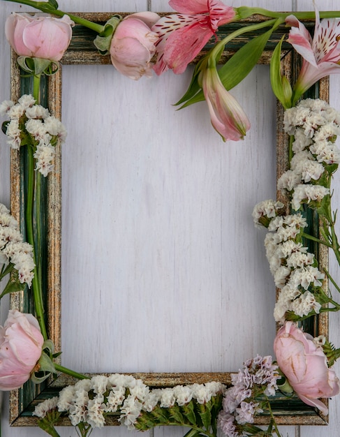 Foto grátis vista superior da moldura dourada esverdeada com flores rosa claro em uma superfície cinza