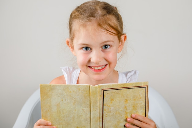 Foto grátis voltar para a escola conceito vista lateral. menina sentada e segurando o livro.