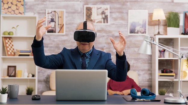 Kostenloses Foto Älterer mann mit virtual-reality-brille im wohnzimmer. frau vor dem fernseher sitzend auf dem sofa im hintergrund.