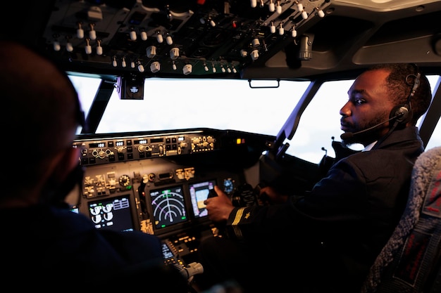 Kostenloses Foto afroamerikanischer pilot, der flugzeugjet fliegt, der teamarbeit mit dem kapitän macht, mit dashboard-befehl und navigation. team von verkehrsflugzeugen, die tasten und hebel auf dem bedienfeld drücken, um abzuheben und zu fliegen.