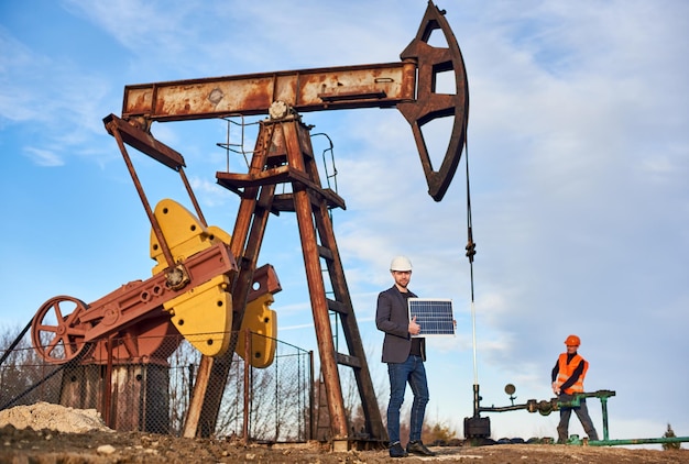 Kostenloses Foto arbeitsprozess eines pumpenhebers und ingenieure im ölfeld an einem sonnigen tag