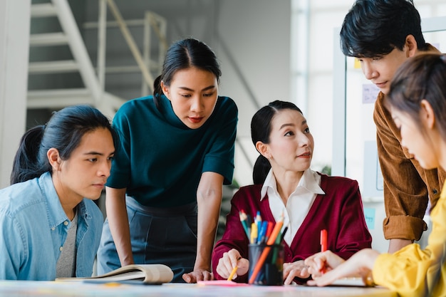 Kostenloses Foto asiatische geschäftsleute und geschäftsfrauen treffen sich mit brainstorming-ideen über kreative webdesign-planungsanwendungen und entwickeln ein vorlagenlayout für ein mobiltelefonprojekt, das in einem kleinen büro zusammenarbeitet.