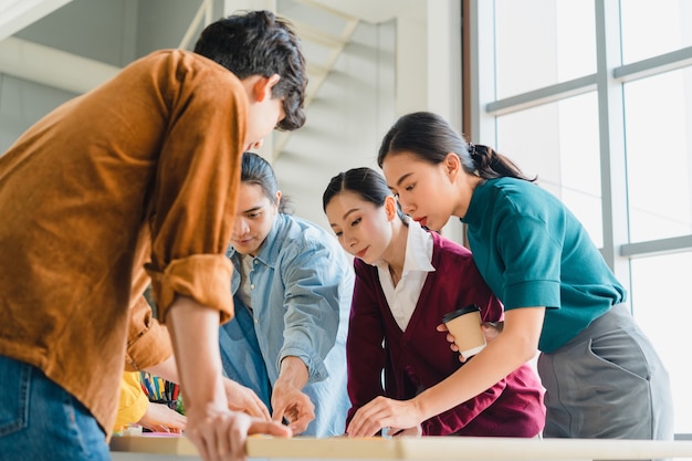 Kostenloses Foto asiatische geschäftsleute und geschäftsfrauen treffen sich mit brainstorming-ideen über kreative webdesign-planungsanwendungen und entwickeln ein vorlagenlayout für ein mobiltelefonprojekt, das in einem kleinen büro zusammenarbeitet.