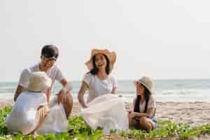 Kostenloses Foto asiatische junge glückliche familienaktivisten, die plastikmüll am strand sammeln. freiwillige aus asien helfen dabei, die natur sauber zu halten und müll aufzuheben. konzept über umweltschutzprobleme.