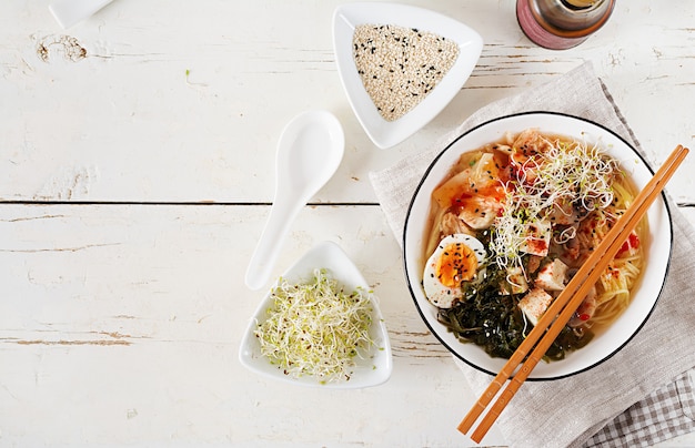 Kostenloses Foto asiatische nudeln miso ramen mit kohl kimchi, meerespflanze, ei, pilzen und käsetofu in der schüssel auf weißem holztisch.