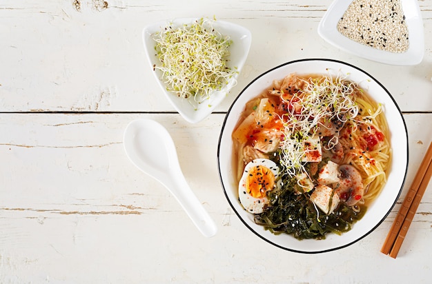 Kostenloses Foto asiatische nudeln miso ramen mit kohl kimchi, meerespflanze, ei, pilzen und käsetofu in der schüssel auf weißem holztisch.