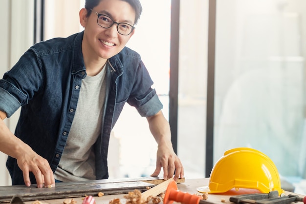 Kostenloses Foto asiatischer männlicher handwerker oder innenarchitekt mit intelligenter, attraktiver handlicher brille konzentriert sich auf die holzbearbeitung am standort