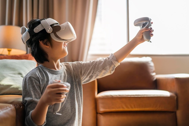 Kostenloses Foto beendendes asiatisches kind, männlicher junge, genießt metaverse-gaming mit tragbarem vr-headset mit steuergriff, das sportspiele online im wohnzimmer zu hause spielt, junger teenager mit vr-technologie