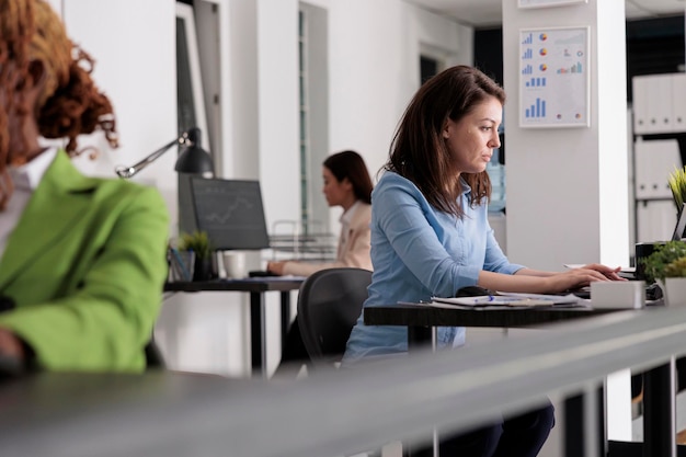 Beschäftigter Firmenmitarbeiter, der am Schreibtisch im Coworking Space arbeitet, Unternehmensleiter am Arbeitsplatz, Seitenansicht. Attraktive ernste Frau, die auf Laptop im modernen Büro tippt, selektiver Fokus