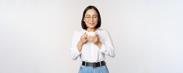 Kostenloses Foto bild einer lächelnden koreanerin, die kaffee im becher riecht und ein köstliches getränk genießt, das über wh steht