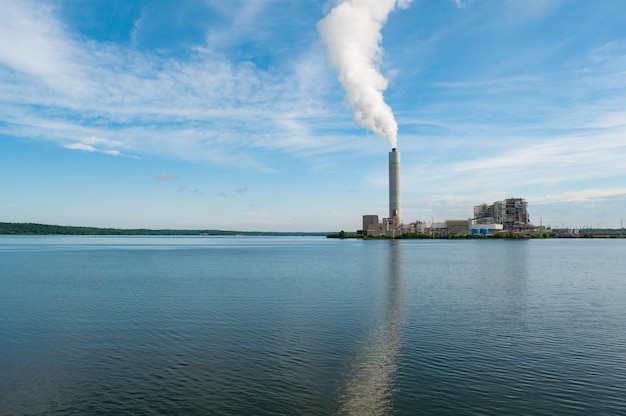 Kostenloses Foto blick auf eine intensive rauchsäule, die aus der wasserlandschaft der fabrikrohre im vordergrund kommt