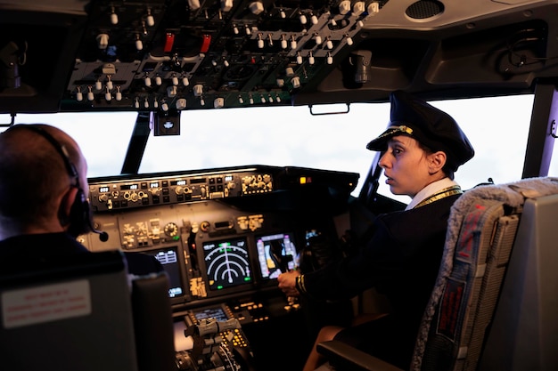 Kostenloses Foto copilotin im einheitlich fliegenden flugzeug mit cockpit-befehlstasten auf dem armaturenbrett der kabine. drücken sie den motor- und radarschalter auf der bedienfeldplatine, um den jet mit verkehrsnavigation zu fliegen.