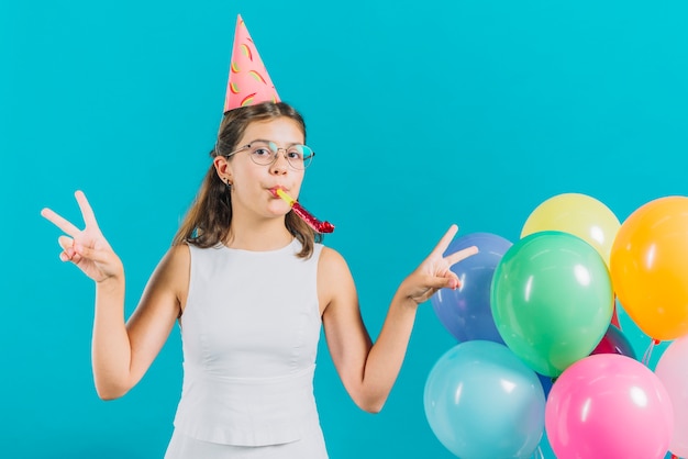 Kostenloses Foto das mädchen, das friedenszeichen nahe bunten ballonen auf türkis gestikuliert, färbte hintergrund