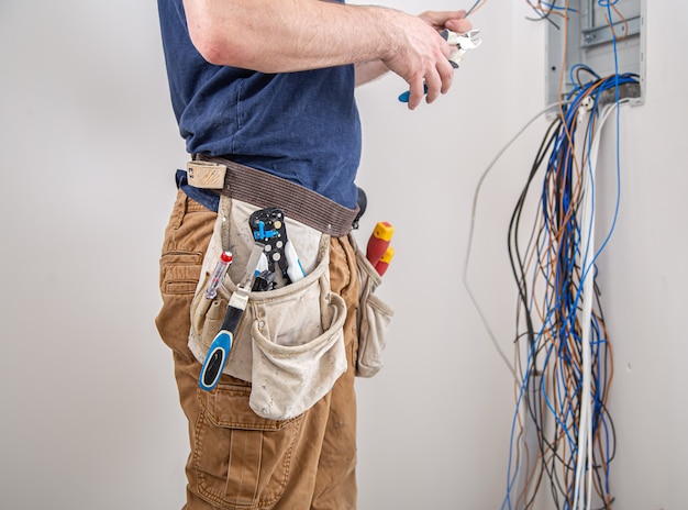 Kostenloses Foto der elektriker bei der arbeit untersucht die kabelverbindung in der elektrischen leitung im rumpf einer industriellen schalttafel. professionell in overalls mit einem elektrikerwerkzeug.