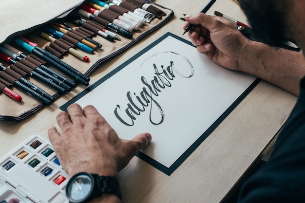 Kostenlose Foto der junge hipster-illustrator-künstler im schwarzen einfachen t-shirt schafft authentische und einzigartige handbeschriftungszeichnung in seinem hellen industriestudio