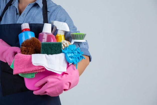 Die Frau hält Reinigungsmittel, Handschuhe und Lappen im Becken an der weißen Wand