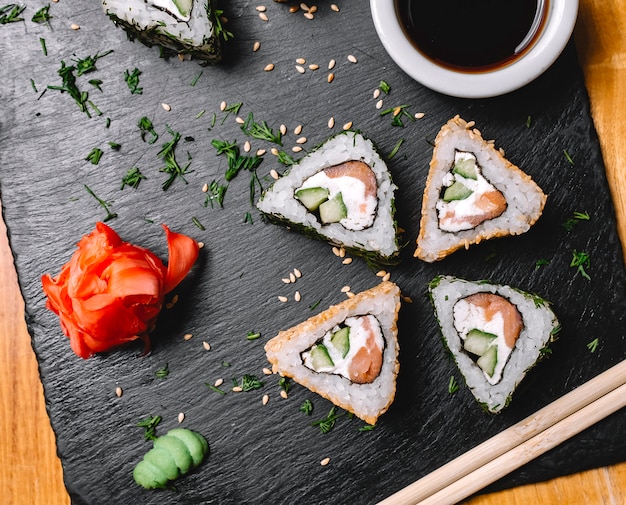 Kostenloses Foto draufsicht sushi-rolle mit lachs frischkäse gurke wasabi ingwer und sojasauce auf einem brett