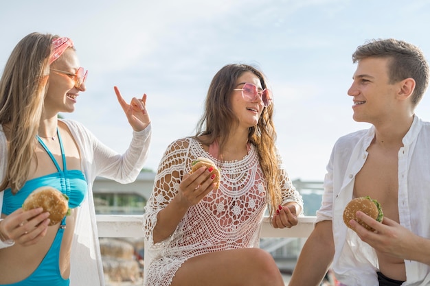 Drei Freunde, die zusammen Burger am Strand essen