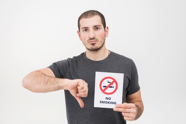 Kostenloses Foto ein junger mann, der das nichtraucherzeichen zeigt daumen unten gegen weißen hintergrund hält