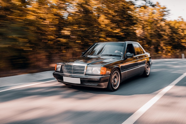 Kostenloses Foto ein schwarzes weinleseauto, das auf die straße sich sehnt über dem wald fährt.