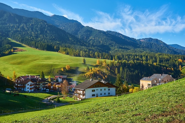 Kostenloses Foto erstaunliche herbstlandschaft im dorf santa maddalena mit bunten kirchenbäumen und wiesen unter aufgehenden sonnenstrahlen dolomiten italien