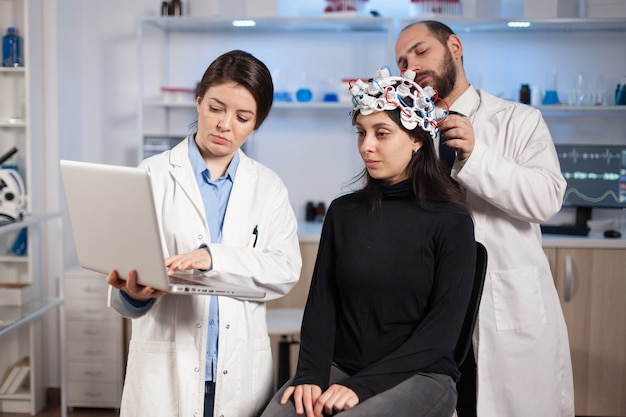 Kostenloses Foto facharzt für neurologe, der notizen auf dem laptop macht und die symptome des patienten fragt, der das high-tech-eeg-headset anpasst. doktorforscher, der das eeg-headset steuert und die gehirnfunktionen und den gesundheitszustand analysiert.