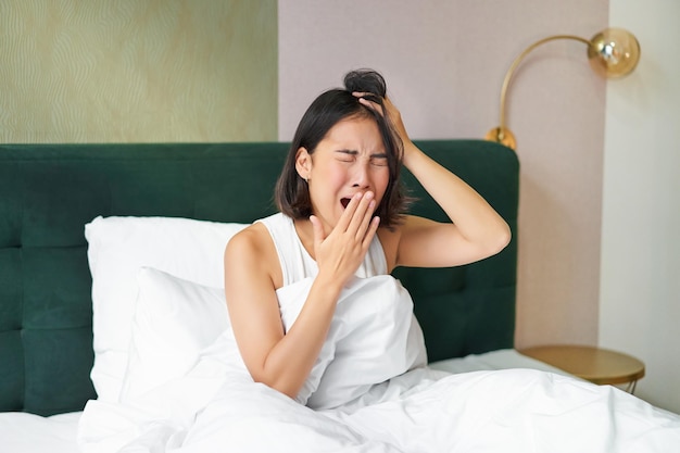 Kostenloses Foto frau, die am frühen morgen nach dem schlafen im schlafzimmer gähnt und grimassen im bett aufwacht