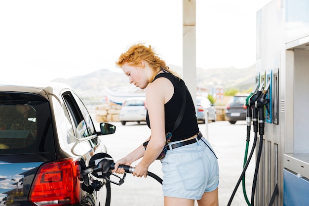 Kostenloses Foto frau, die auto mit benzin an der tankstelle betankt