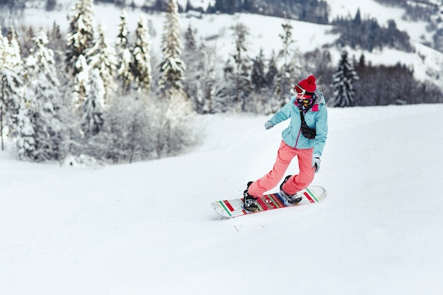 Kostenloses Foto frau im skianzug schaut über ihrer schulter, die den hügel auf ihrem snowboard hinuntergeht