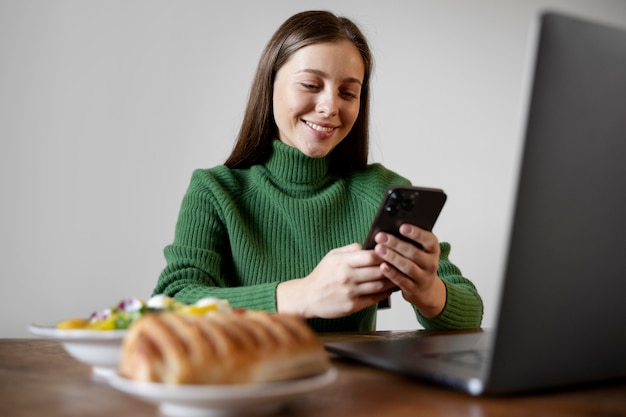 Frau schaut auf ihr Smartphone, während sie ihr Essen isst