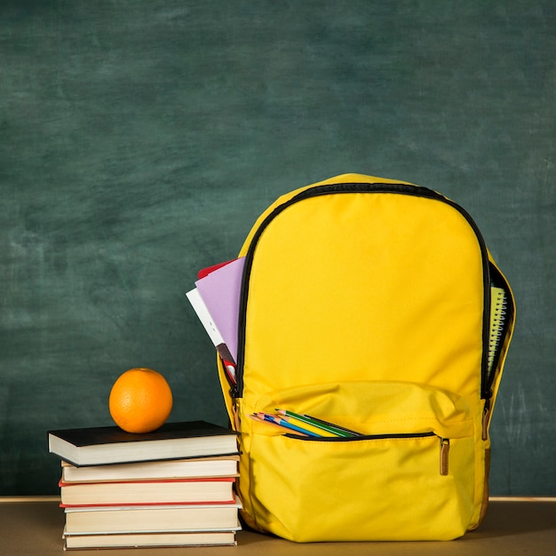 Gelber Rucksack, Stapel Bücher und Orange