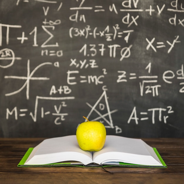 Kostenloses Foto geöffnetes buch mit apfel auf schreibtisch nahe tafel